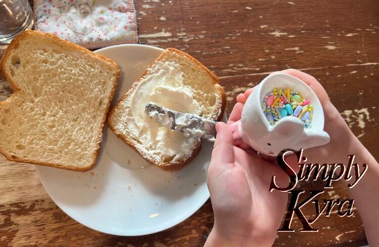 One piece of toast is spread with cream cheese while the second one remains plain. The bunny is held up for the photo. 