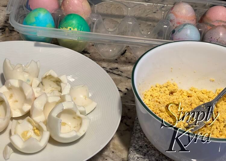 Image shows a plastic egg carton in the background with four eggs on either end and four missing slots in the center. In the foreground is a plate with yolk speckled zigzagged half egg whites and a bowl of crumbly yellow to the right. 