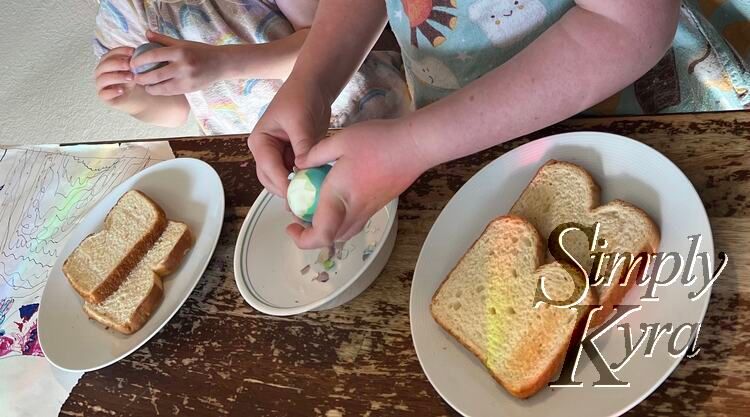 Image shows the girls side by side each with a plate of two pieces of toast and a bowl between for the egg shells. 