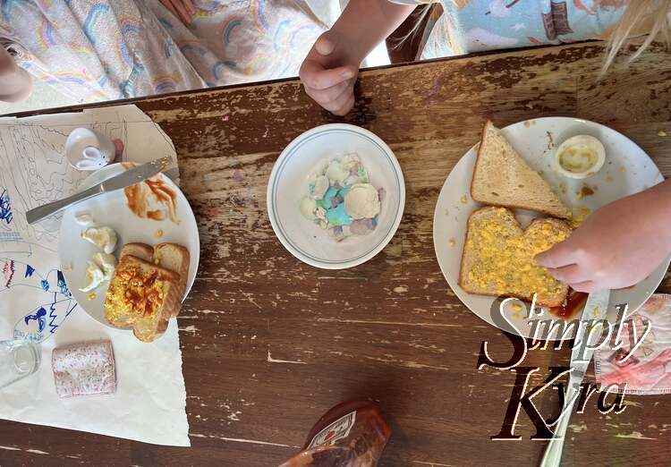 Image taken from above shows a bowl of dyed egg shells with a plate on either side with toast, crushed yolks, egg white pieces, and ketchup.