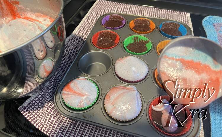 Same bowl as the previous photo but now there's a single cupcake pan missing a liner. This time around a red, blue, and lavender angel food mix is being poured into the brownie cupcake liners.