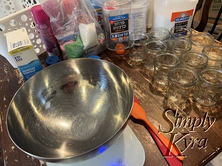 Image shows a metal bowl sitting on a scale. Two spatula sit beside it with opened jam jars to the right of it. In the back sits all the ingredients. 