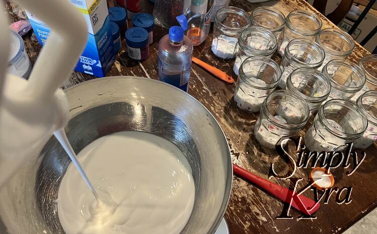 Image shows glue being poured into the metal bowl. In the background the jars are partially filled with white rainbow specked slime.