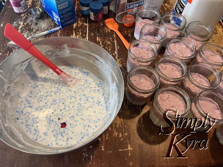 Image shows the blue specked white slime in a bowl with a splotch of red food dye in the center-ish. Off to the side are the first two batches already within the jars.