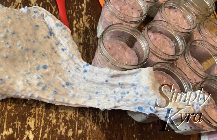 The slime is spread from the spot on the table to the jars to better highlight the blue elements within it. The jars are filled with the white bottom and lavender layers already. 