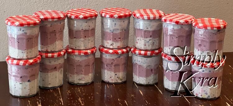 Image shows a curved row of seven slime filled jam jars across each topped with another one making fourteen. The top of each has a white and red plaid lid. 