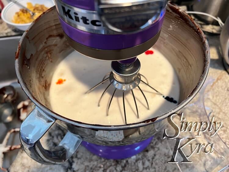 Image shows the bowl of a stand mixer looking down with the whisk down and turned off. There's a red drop in the upper right, blue in lower right, and yellow on center left. 
