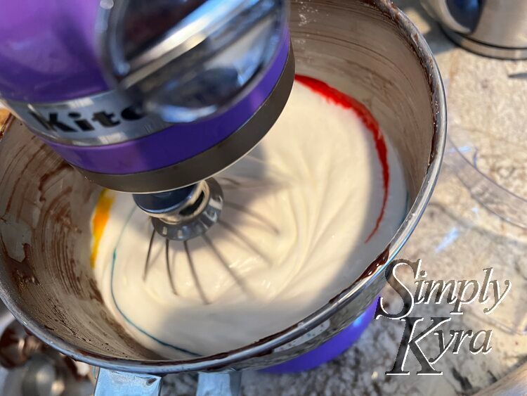 Image shows the bowl of a stand mixer looking down with the whisk down, turned on, and blurred. The colors have streaked along the outside.