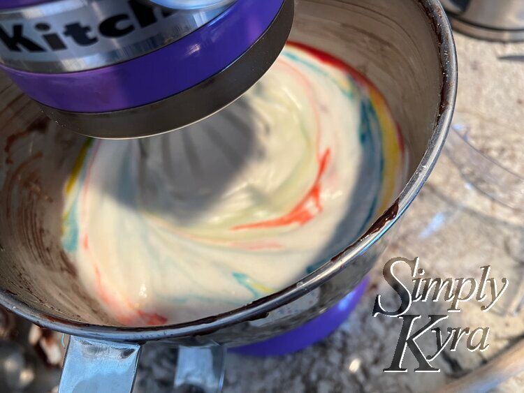 Image shows the bowl of a stand mixer looking down with the whisk down, turned on, and blurred. The colors are there in bit and starts the whole way around.