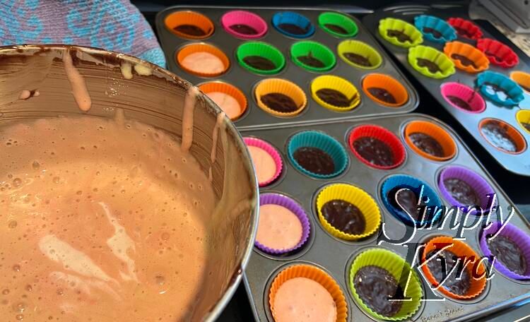 Image shows a bowl of brownie streaked brown-ish angel food cake to the left and three cupcake pans to the right. The colorful liners are half filled with partially cooked brownies with the one on the far left two thirds filled with the angel food mix. 