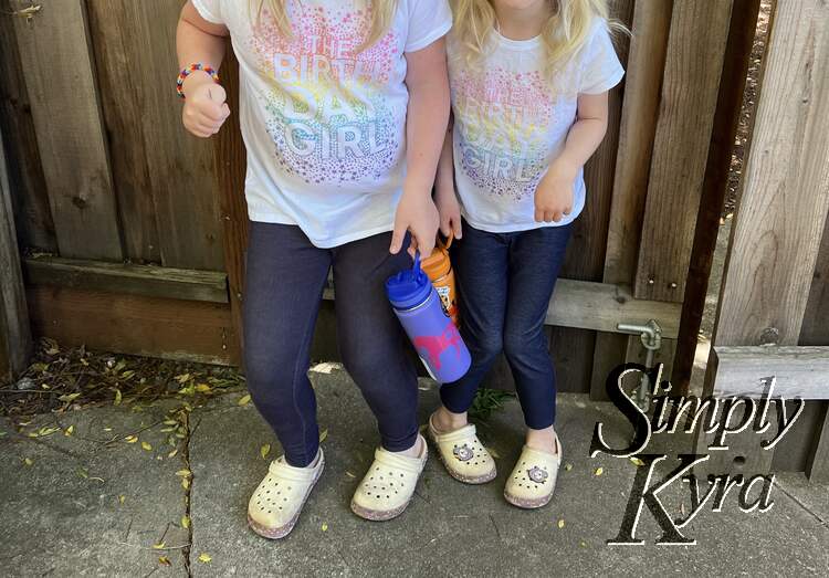 Image shows the two girls side by side in matching "Then birthday girl" shirts holding their water bottles. 