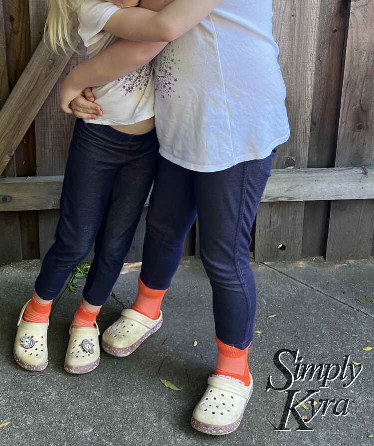 Image is similar as before but not they have bright orange socks on. Ada is trying to lift Zoey.