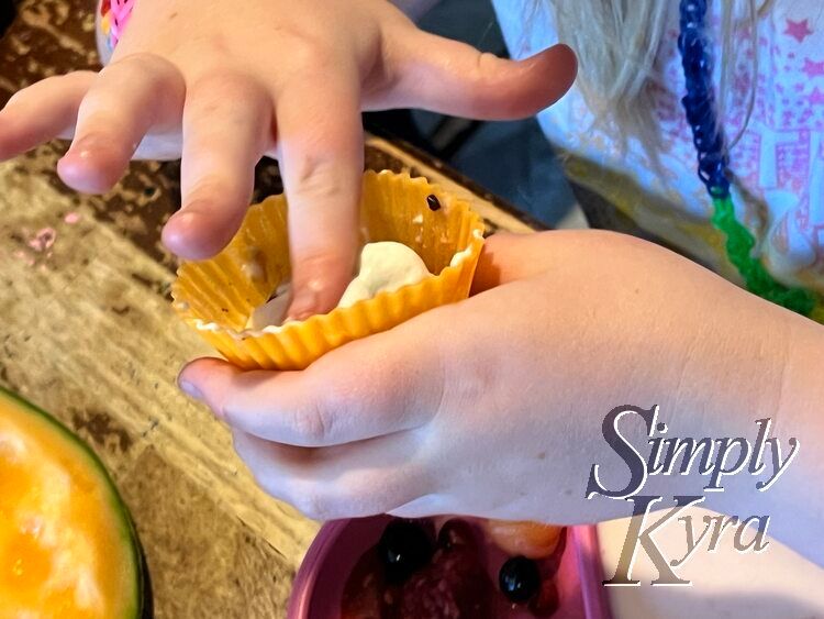 Ada holds her orange liner above a similarly filled play while squishing down the whip cream inside. 