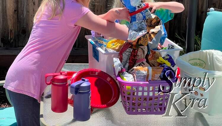 Two baskets of snacks, water bottles, paper plates, and two happy kids at the patio furniture outside. 