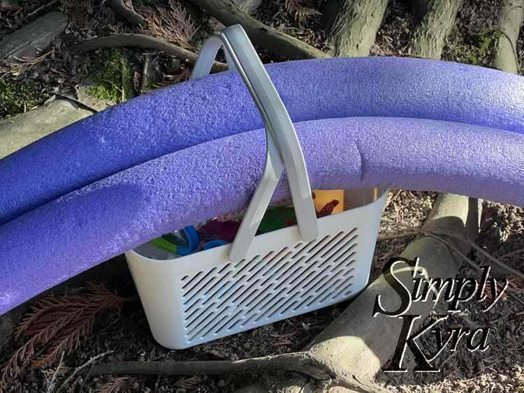 Image shows the basket set on a tree root with the purple pool noodles stretched out but set in place with the handle. 