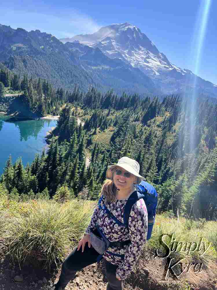 Image shows me smiling in the foreground with Mount Rainier/Tahoma in the background and lake Eunice to the left in the mid-ground.