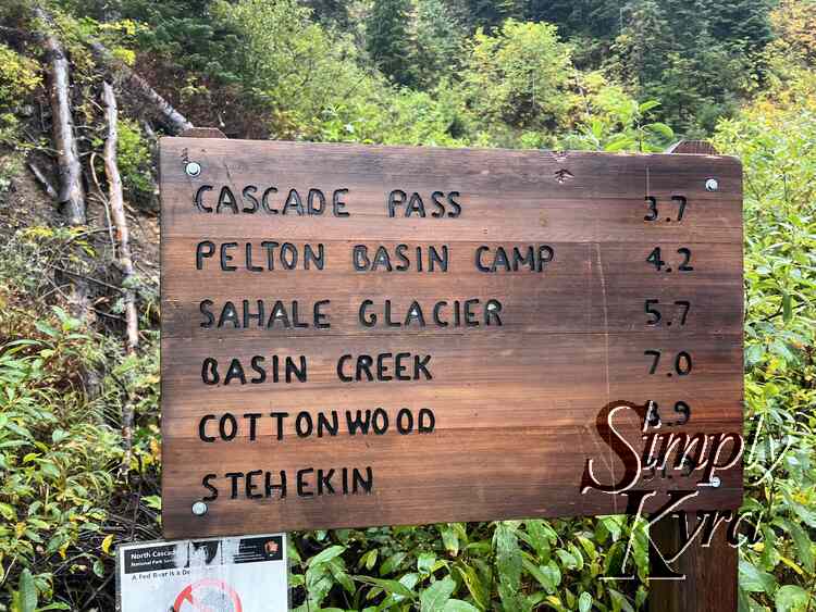 Sign at the trailhead listing the trail destinations and distance in miles. Cascade pass is the smallest at 3.7 while Stehekin is the longest at over 30 miles away. 