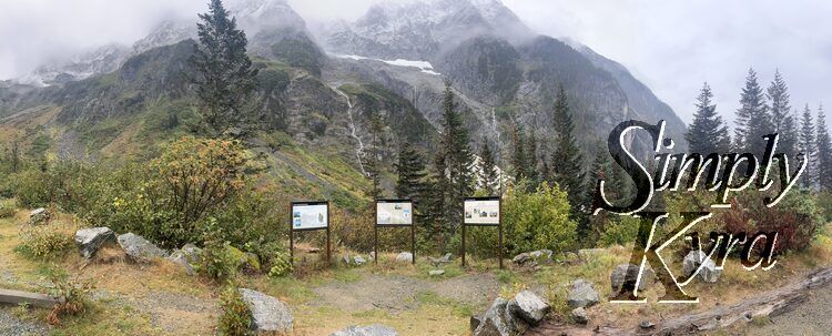 Panorama photo from the parking lot showing the informational posters with the mountains and streams in the background. 