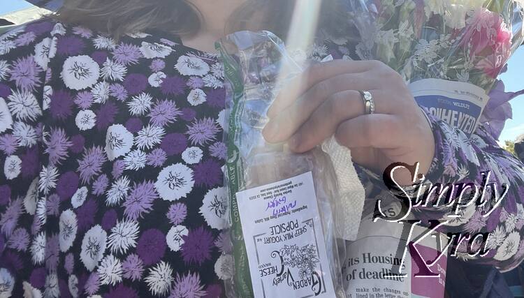 Image is a closeup of me holding a yogurt popsicle and bundle of flowers with a sunbeam in front. 