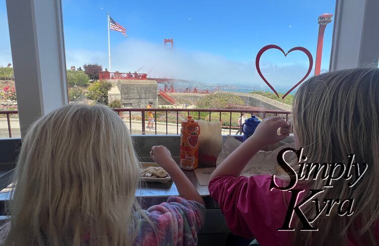 Image shows the kids eating while looking through a window with a heard on it showing the Golden Gate Bridge. 
