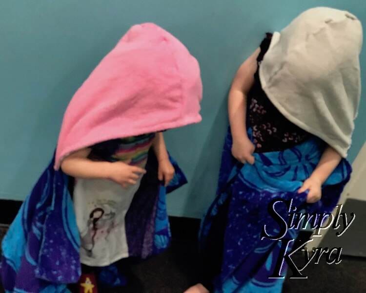 Image is a bit blurred but shows the girls with the hooded towel on them over their clothing while they look down at the new towel. 