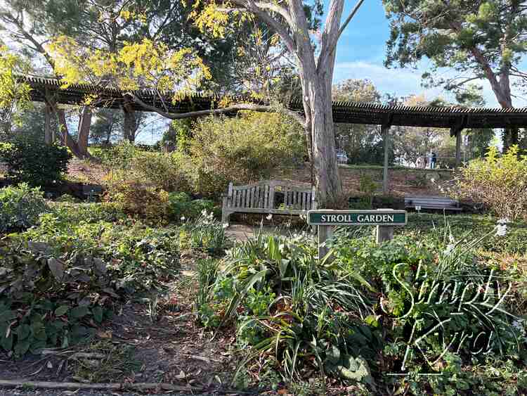 Image shows a sigh saying "stroll garden" with a bench under a tree behind.  