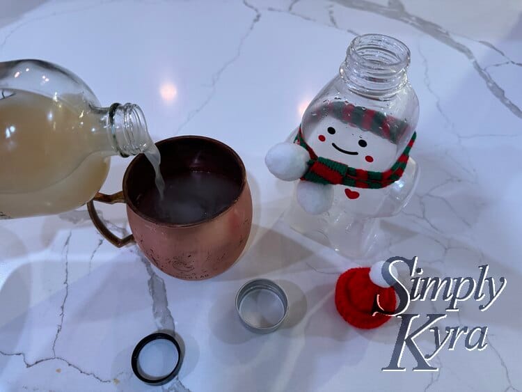 Image shows an open and emptied festive ginger beer bottle standing next to an ice added Ginger Lab mule glass getting topped up with more ginger beer. 