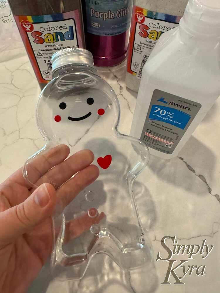 Image shows me holding the bottle on its side with the glitter, two sand colors, and isopropyl alcohol in the background.