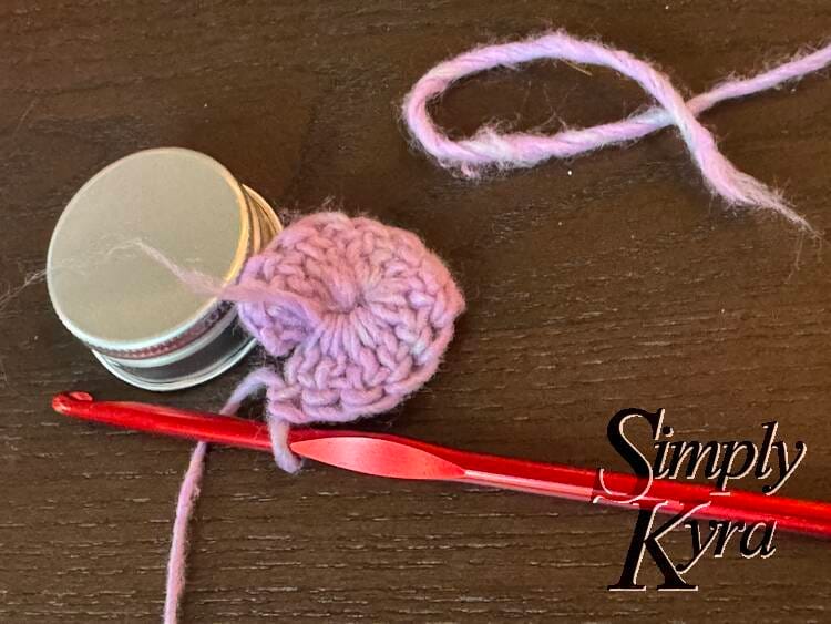 Image shows the circle almost complete with a red crochet hook still attached leaned up against the lid. It the back is the ripped off piece. 