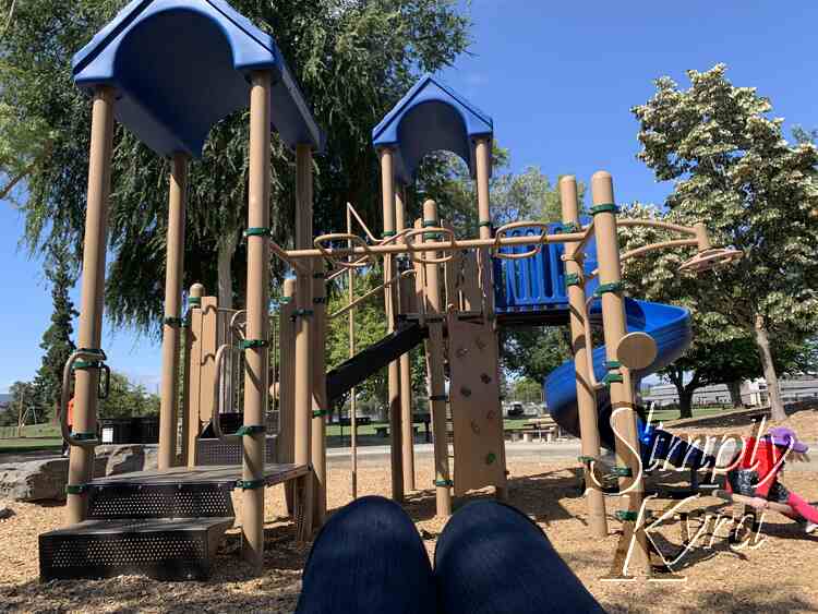 Image shows my knees as I sit and watch the kids spin or run she equipment course... how they were taking turns on the spinning that day.