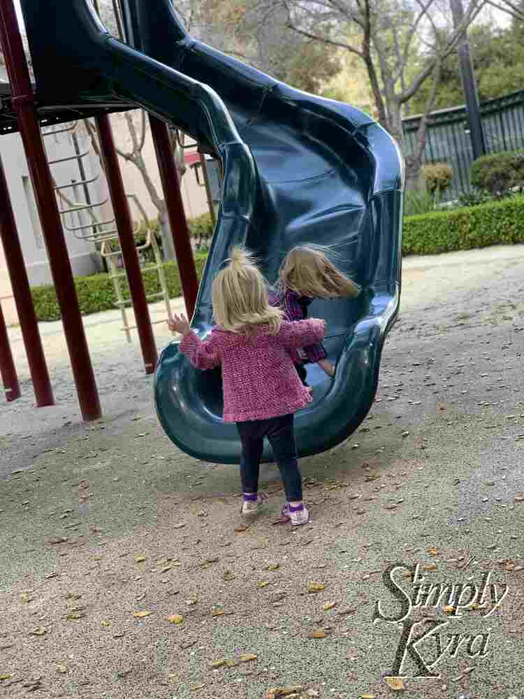 Image shows Ada at the bottom of a tall slide with Zoey excitedly at the bottom. 