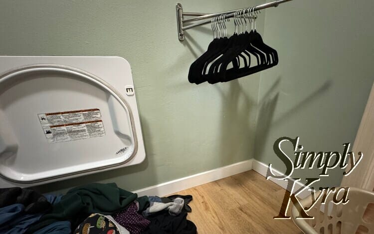 Image shows the laundry room with the clean unfolded laundry to the left, empty basket to the right, and empty hangers directly in front on the bar.