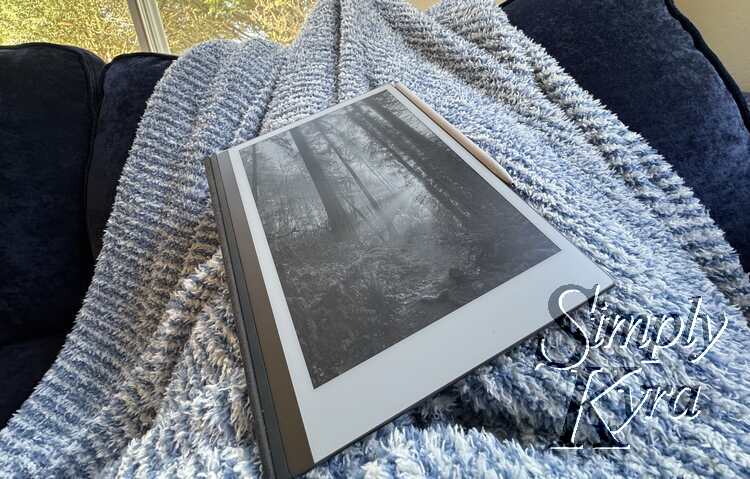 Image shows the reMarkable on my blanket covered lap showing sunlight between the trees.