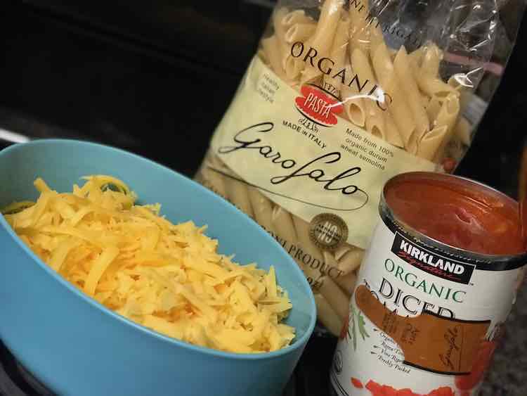 A package of pasta, grated cheddar cheese, and a can of diced tomatoes.