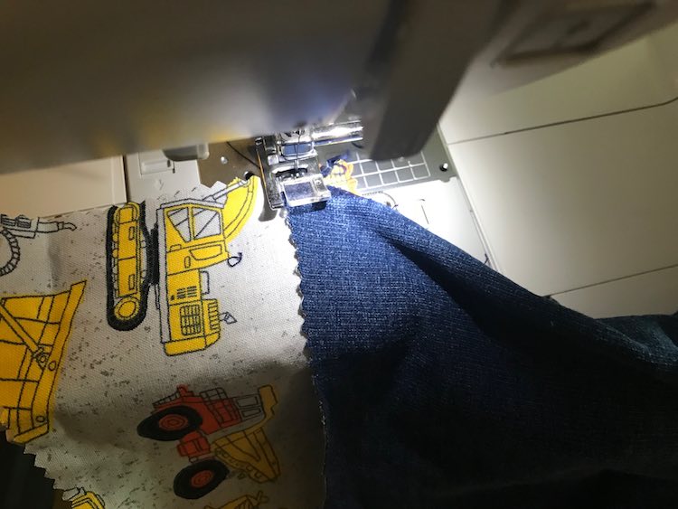 I then lined up the woven construction vehicle fabric underneath the top of the pants so both were right side up. I made sure the construction vehicles stuck out a bit further than the side of the jeans.