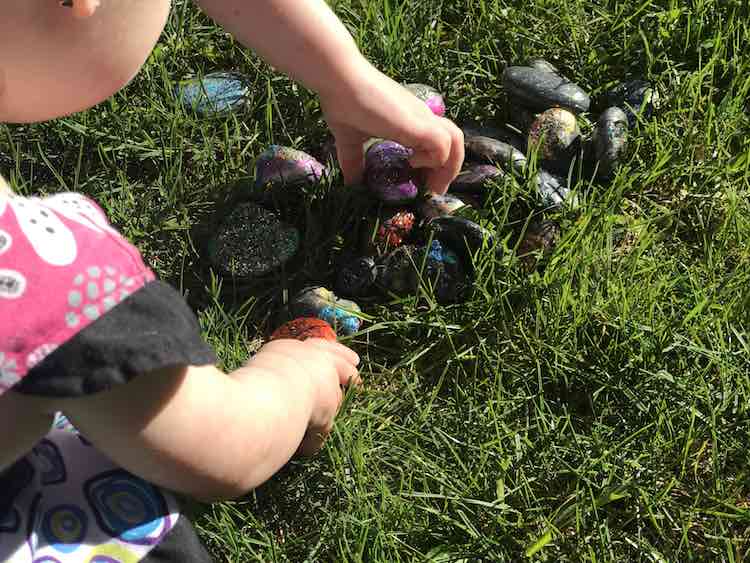 The painted rocks nestled in green grass. Both girls are leaned over picking their favorites.