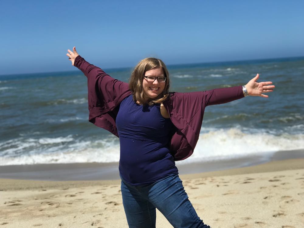 Arms spread and up in front of the ocean.