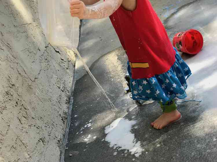 Zoey holding up the oobleck container as threads of it drip down.