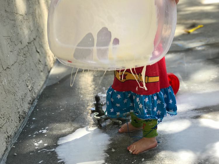 Zoey holding up the oobleck container as threads of it drip down.