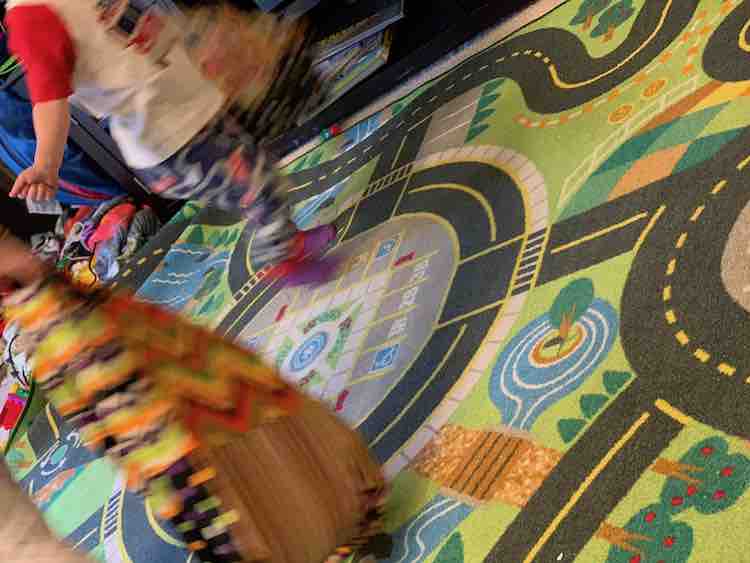 Kids running around the road track floor mat while carrying the market bags.