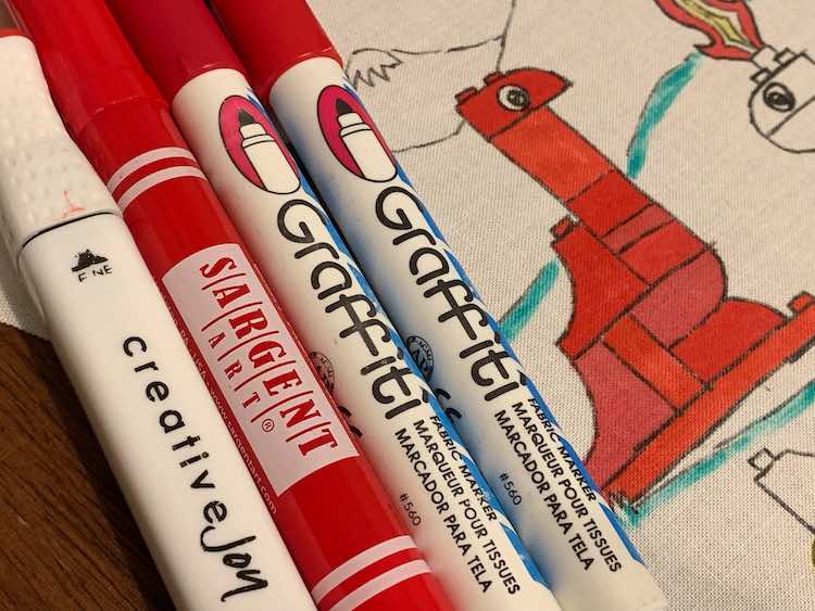 Three brands and four individual fabric markers used to color in the red dinosaur in the background.
