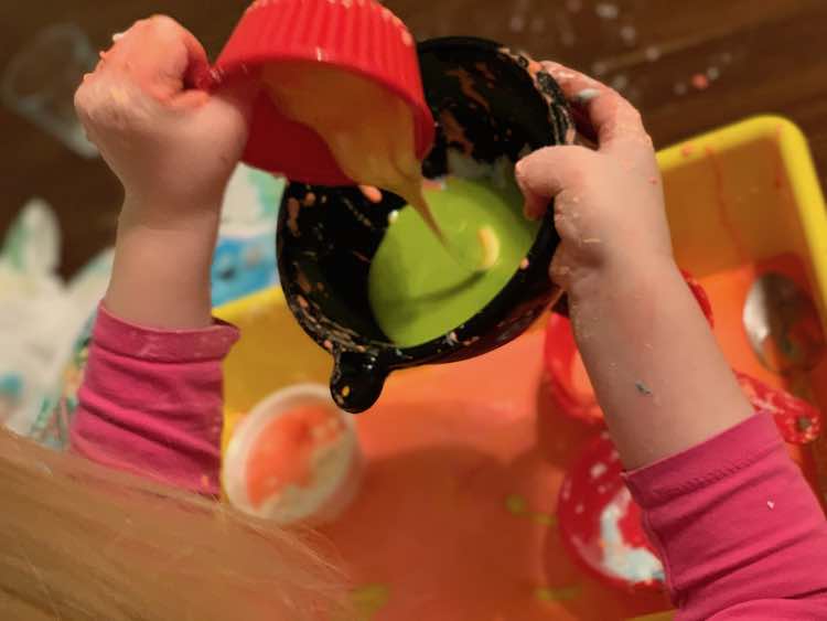 Mixing the red in the funnel with the yellow oobleck she was pouring to make green.