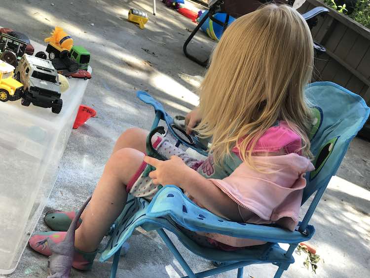 Ada sitting in her chair pretend playing with the vehicles.