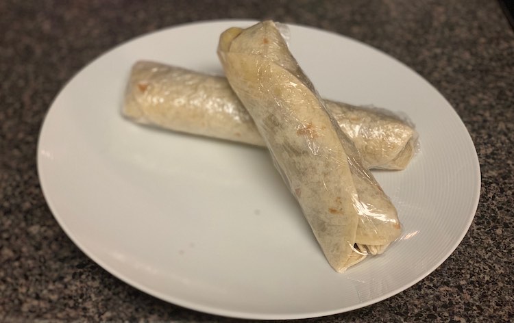 Two made banana wraps individually wrapped with plastic wrap.