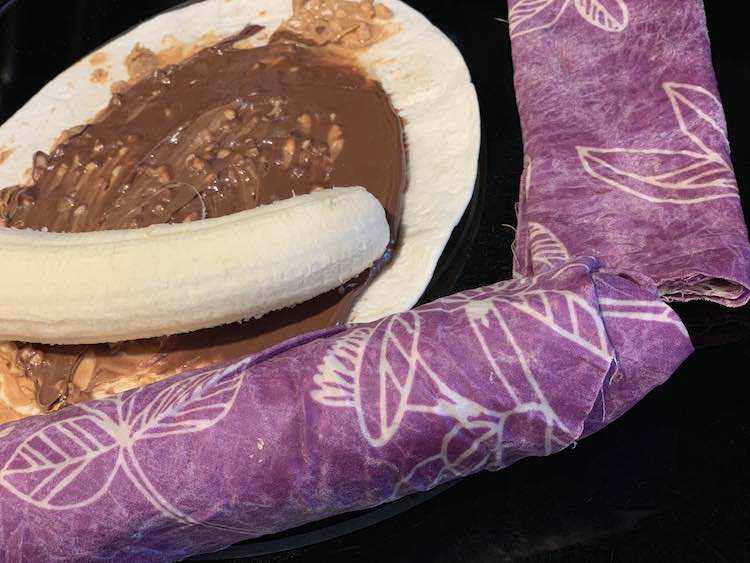 Banana about to be wrapped in chunky peanut butter, Nutella, and the tortilla wrap. Finished and fully wrapped wrap beside the half finished one.