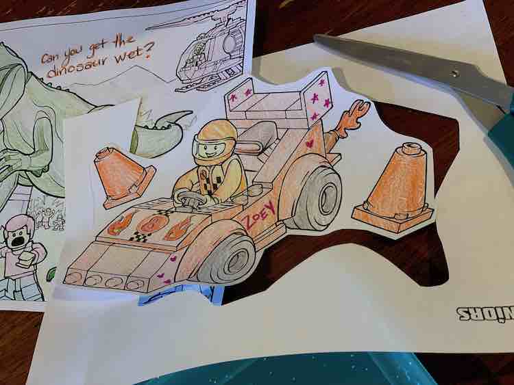 Cut out and colored race car in the foreground with the outer paper, scissors, and a whole dinosaur coloring page in the background.