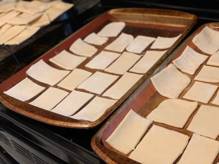 Pizza crust cut out and ready to go into the oven. In the background you can see the baked pizza crust on a cooling rack.