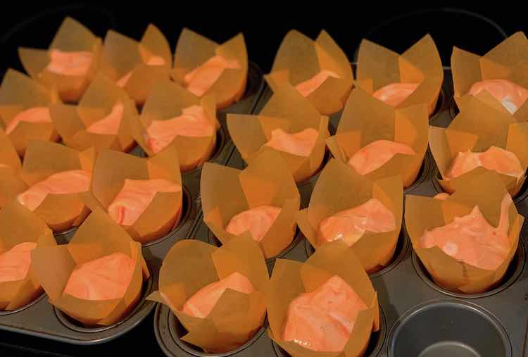 Orange paper tulip cupcake wrappers filled with orange angel food cake. One recessed hole in the cupcake tin is left empty.