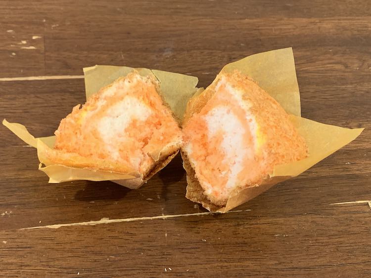 Image of a paper lined orange cupcake cut in half so you can see bits of white and yellow.