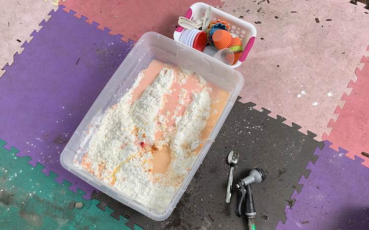 All the ingredients added to the bin (cornstarch, food dye, and water). The cornstarch is rising out from orange/pink water.
